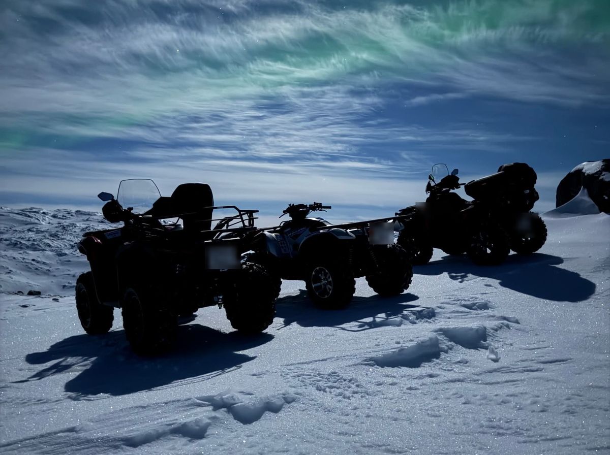ATV'er parkeret i sneen under nordlys